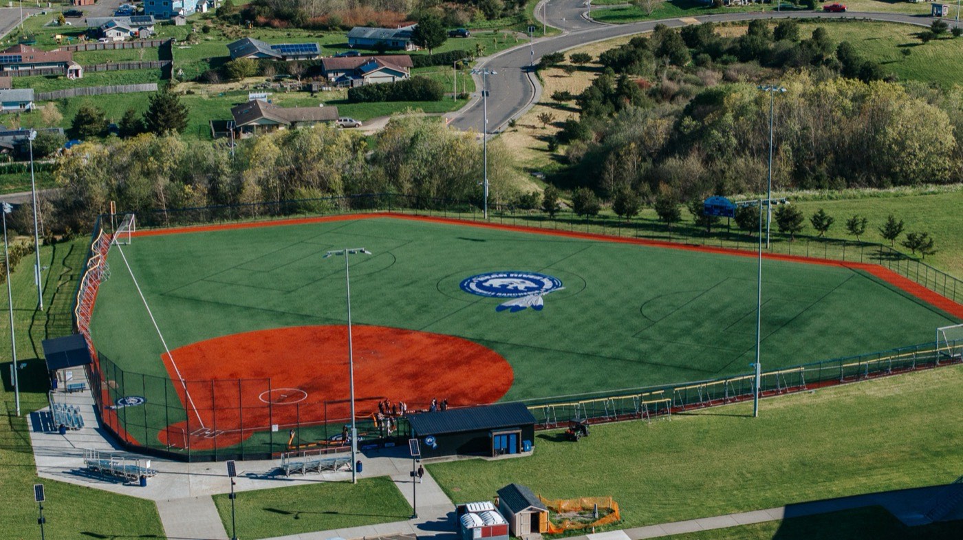 Drone shot of a chain link-fenced baseball complex with bleachers and dugouts, Humboldt County area