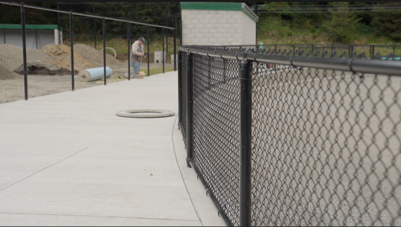 Black chain link fence around a commercial concrete utility pad on the North Coast