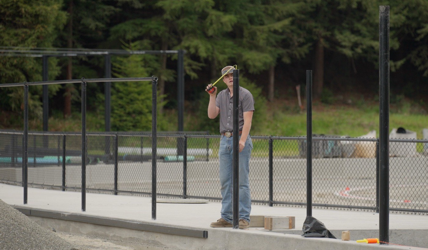 Humboldt Fence crew member measuring during a chain link install on a poured-concrete pad