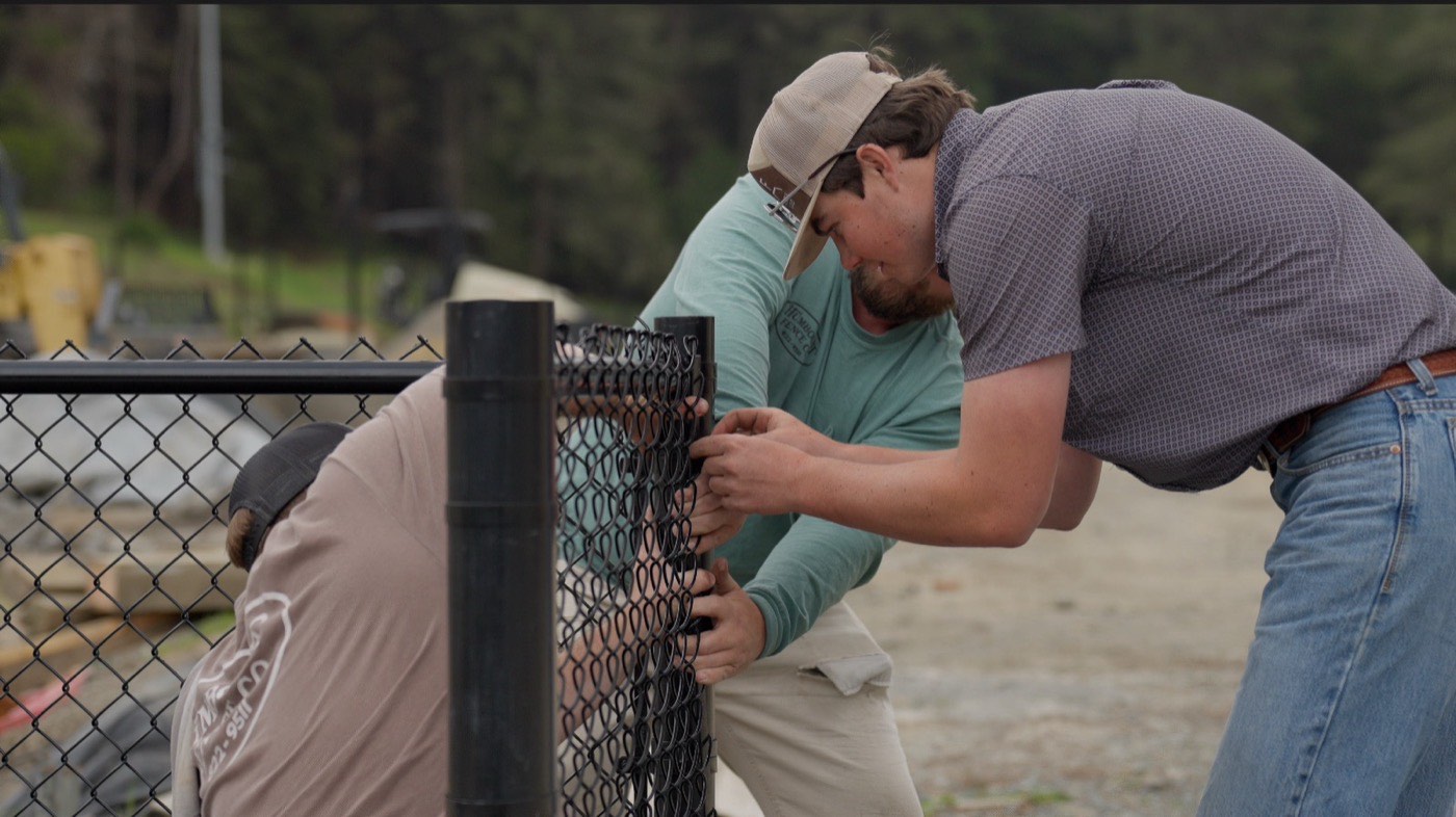 Two Humboldt Fence installers tensioning chain link mesh on a commercial install